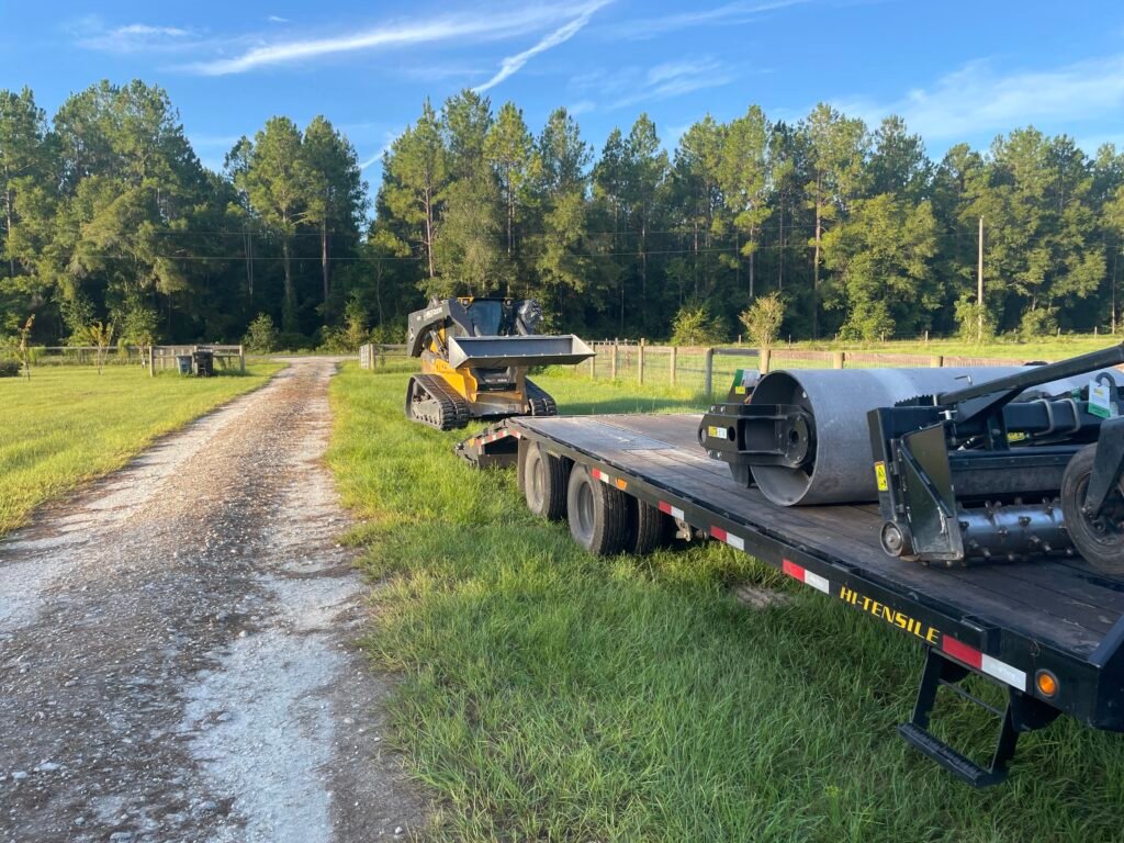 Excavation equipment and trailer on gravel driveway surrounded by green grass and trees, relevant to outdoor services and land development in Florida.