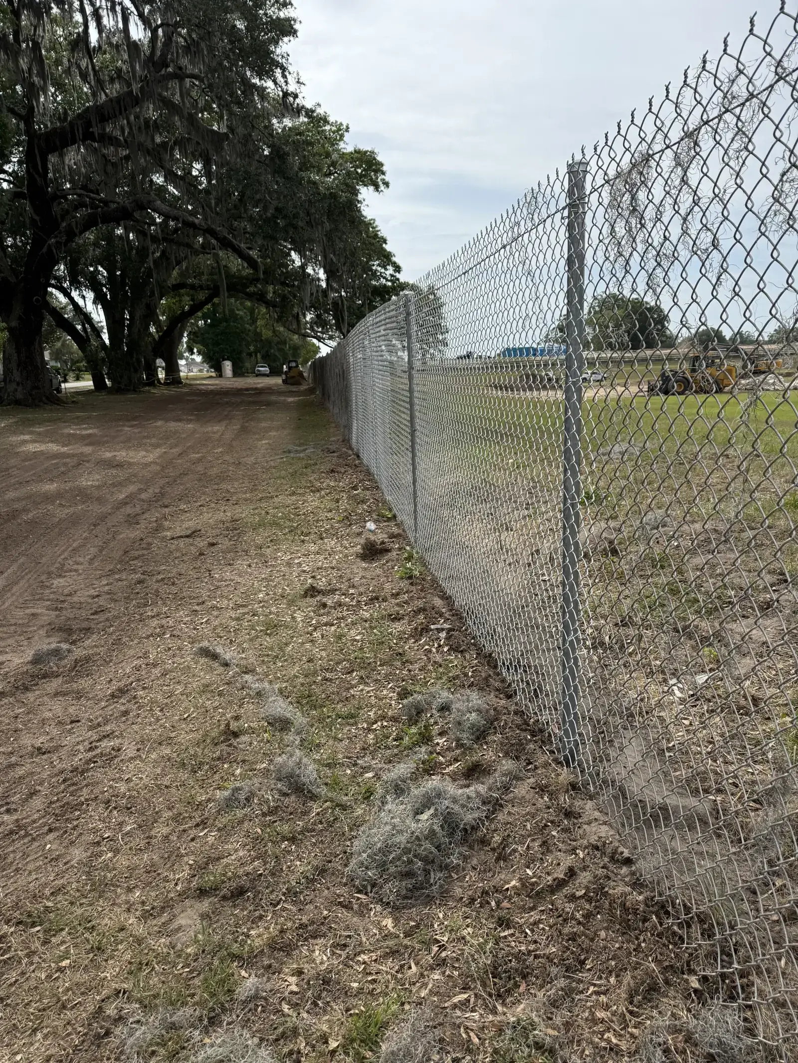 Chain link fence installation along a wooded path, showcasing Bell's Outdoor Services' fencing expertise in a Florida outdoor setting.