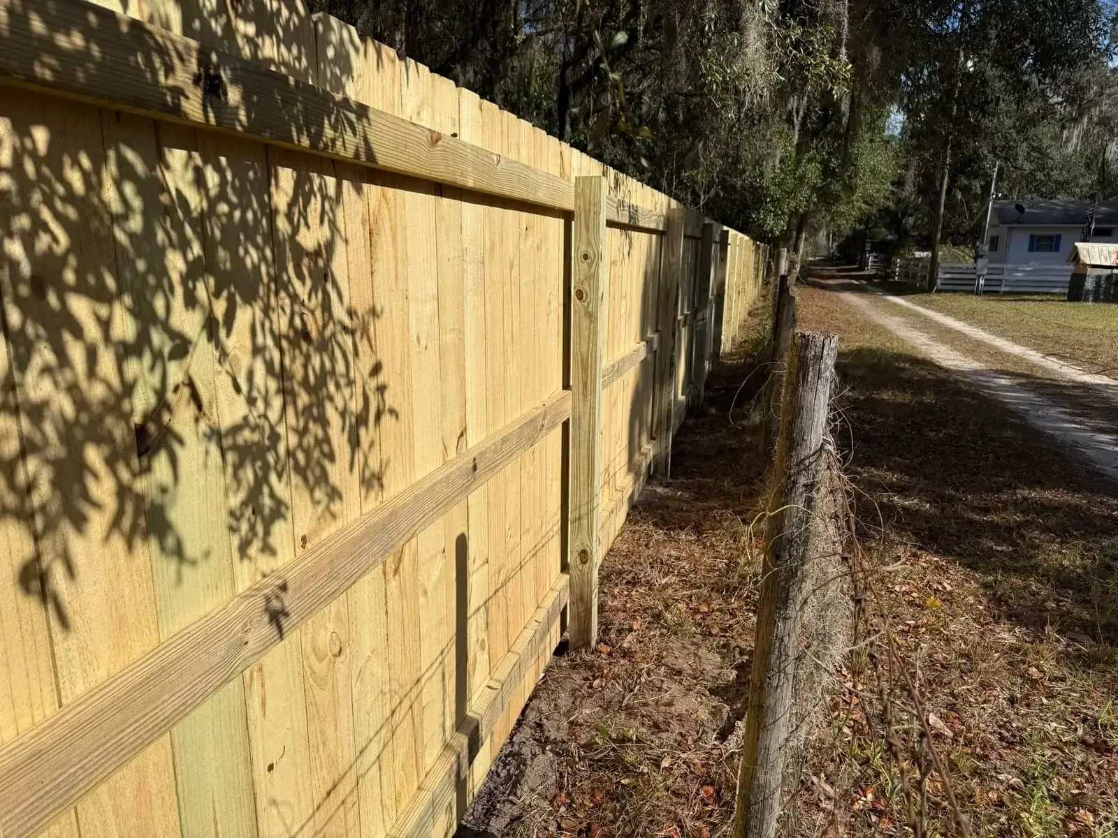 Close-up side view of a newly installed, natural wood privacy fence along a dirt road