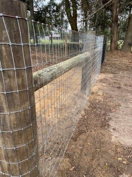 Woven wire fence installation with wooden posts in a Florida outdoor setting, showcasing Bell's Outdoor Services' fencing expertise.