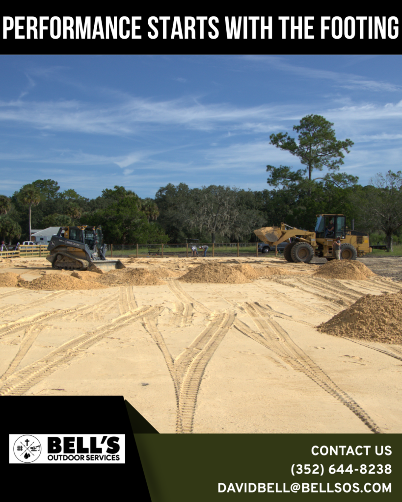 Construction site with heavy machinery, including a bulldozer and loader, grading land for an equestrian arena, with sandy terrain and trees in the background, featuring Bell’s Outdoor Services branding.